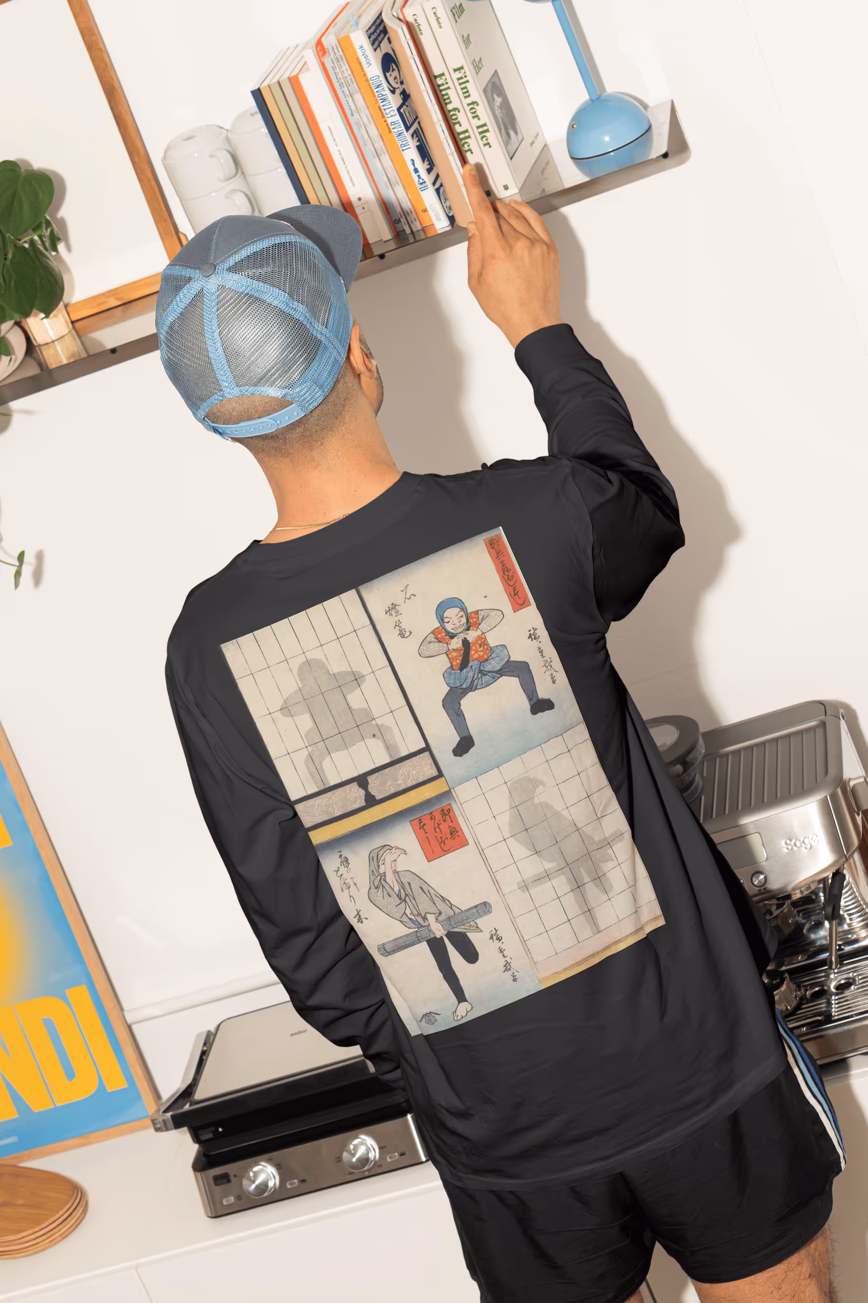 Person mit schwarzem Longsleeve mit japanischem Comic-Motiv am Rücken greift nach Buch im Regal.