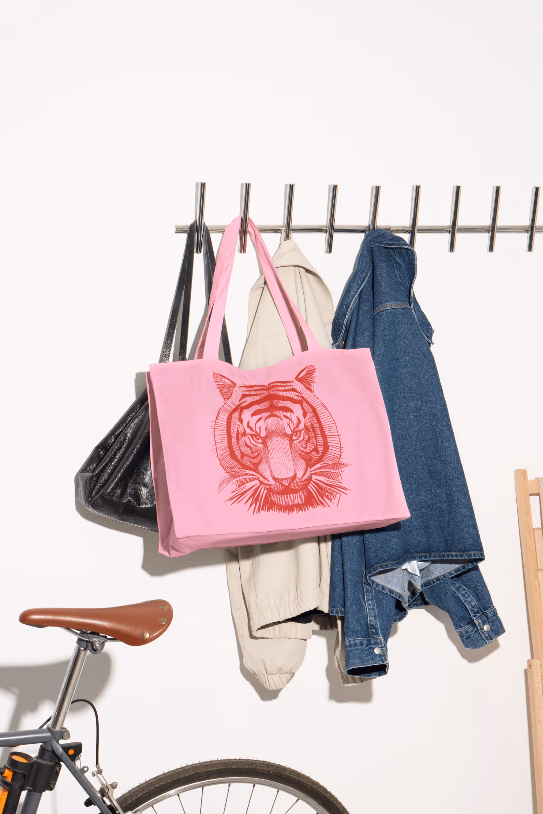Rosa Tragetasche mit rotem Tigerkopf-Print hängt an Garderobe neben Jacken.