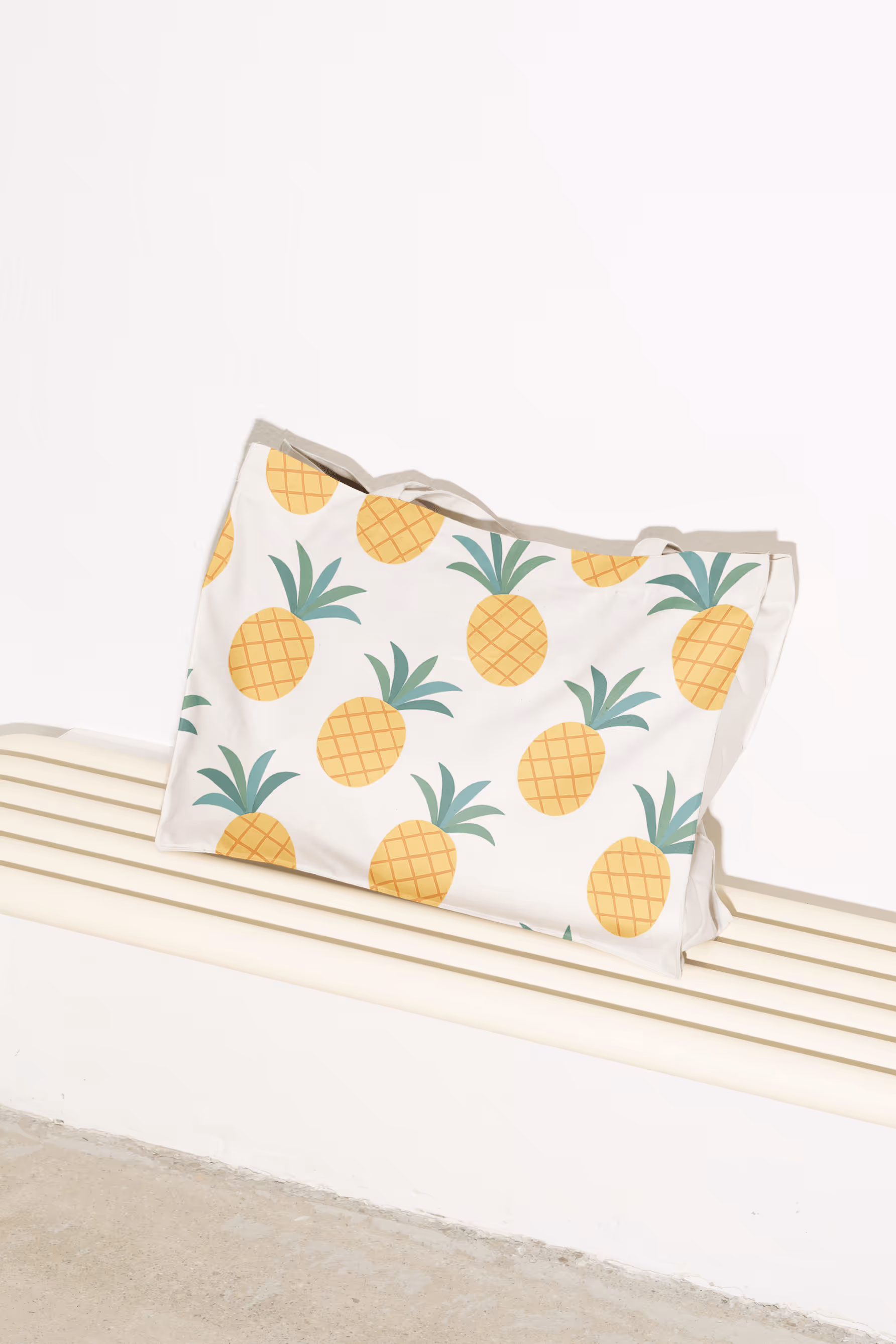 Grosse Stofftasche mit Ananas-Muster auf heller Sitzbank.