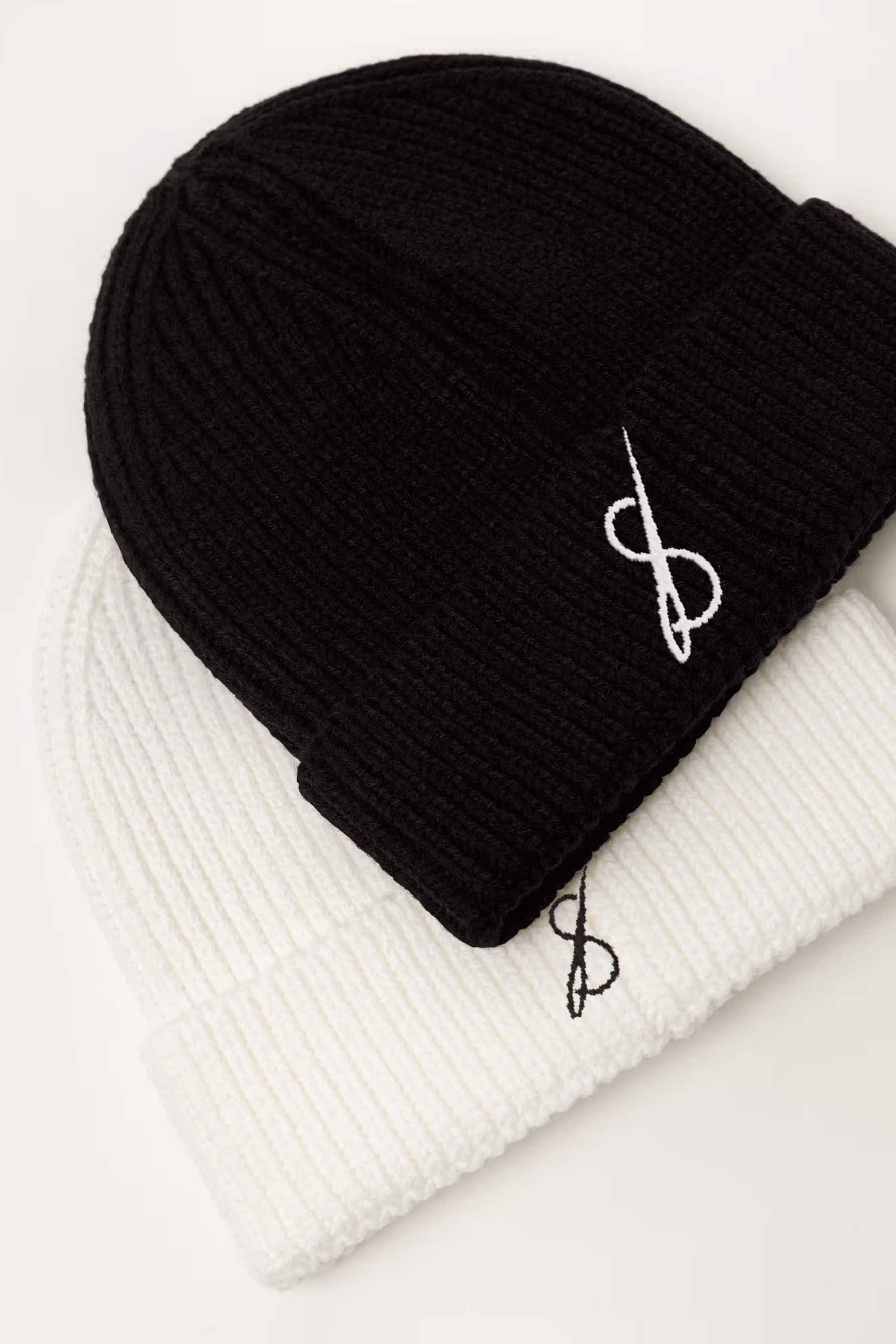Zwei Strickmützen, eine schwarz und eine weiss, beide mit weissem bzw. schwarzem Sticklogo.