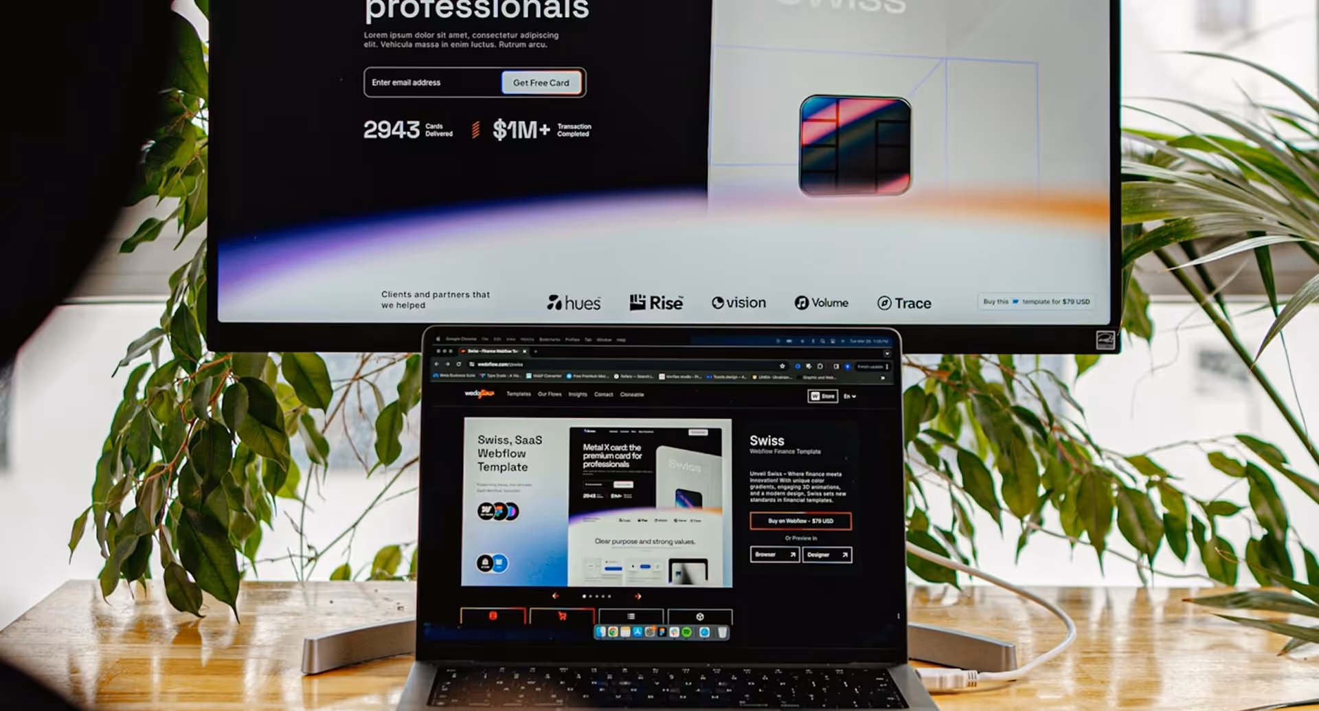 Laptop and large monitor displaying a Swiss SaaS Webflow template on a wooden desk with green plants nearby.