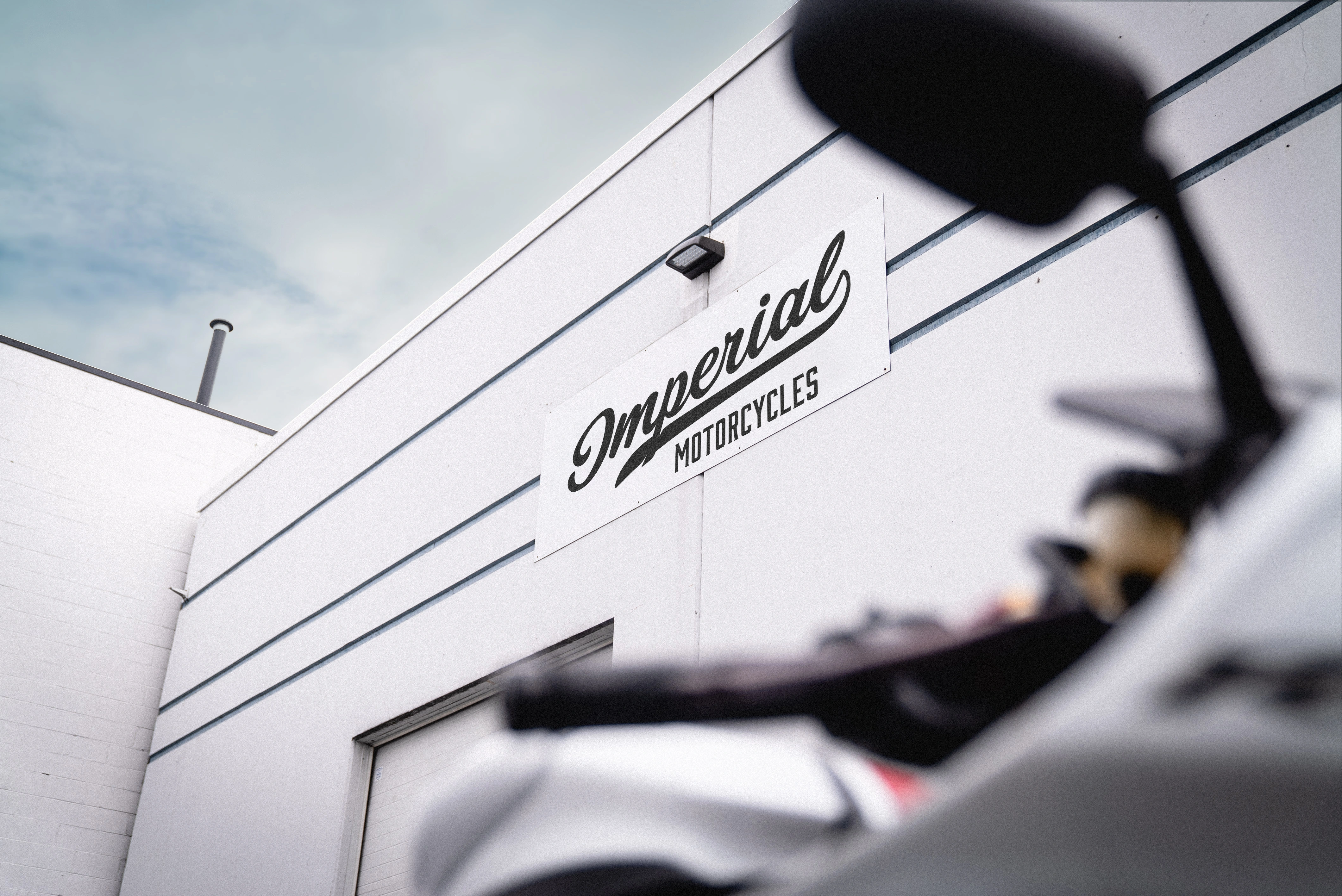 Exterior of a white building with a sign reading 'Imperial Motorcycles' and a blurred motorcycle mirror in the foreground.