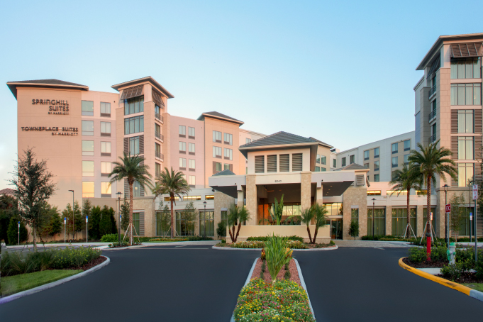 Front view of SpringHill Suites by Marriott hotel with a clear blue sky and palm trees lining the driveway.