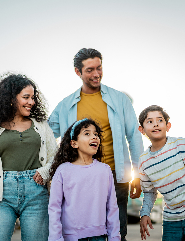 Smiling family of four outdoors at sunset, including a man, woman, and two children looking excited.