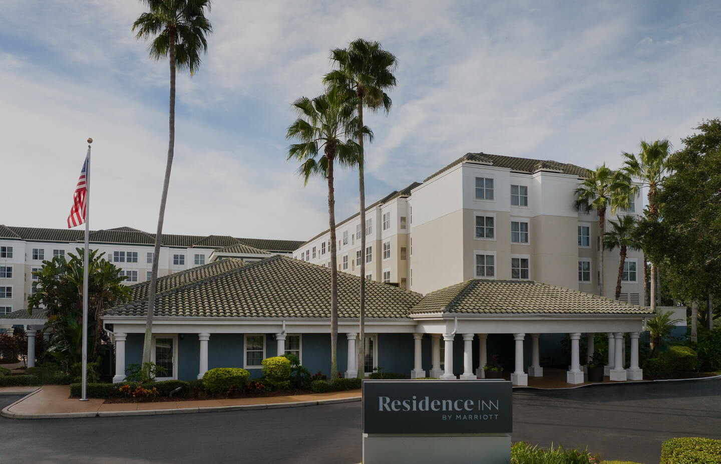 Residence Inn by Marriott hotel building with tiled roofs, palm trees, and an American flag in front.