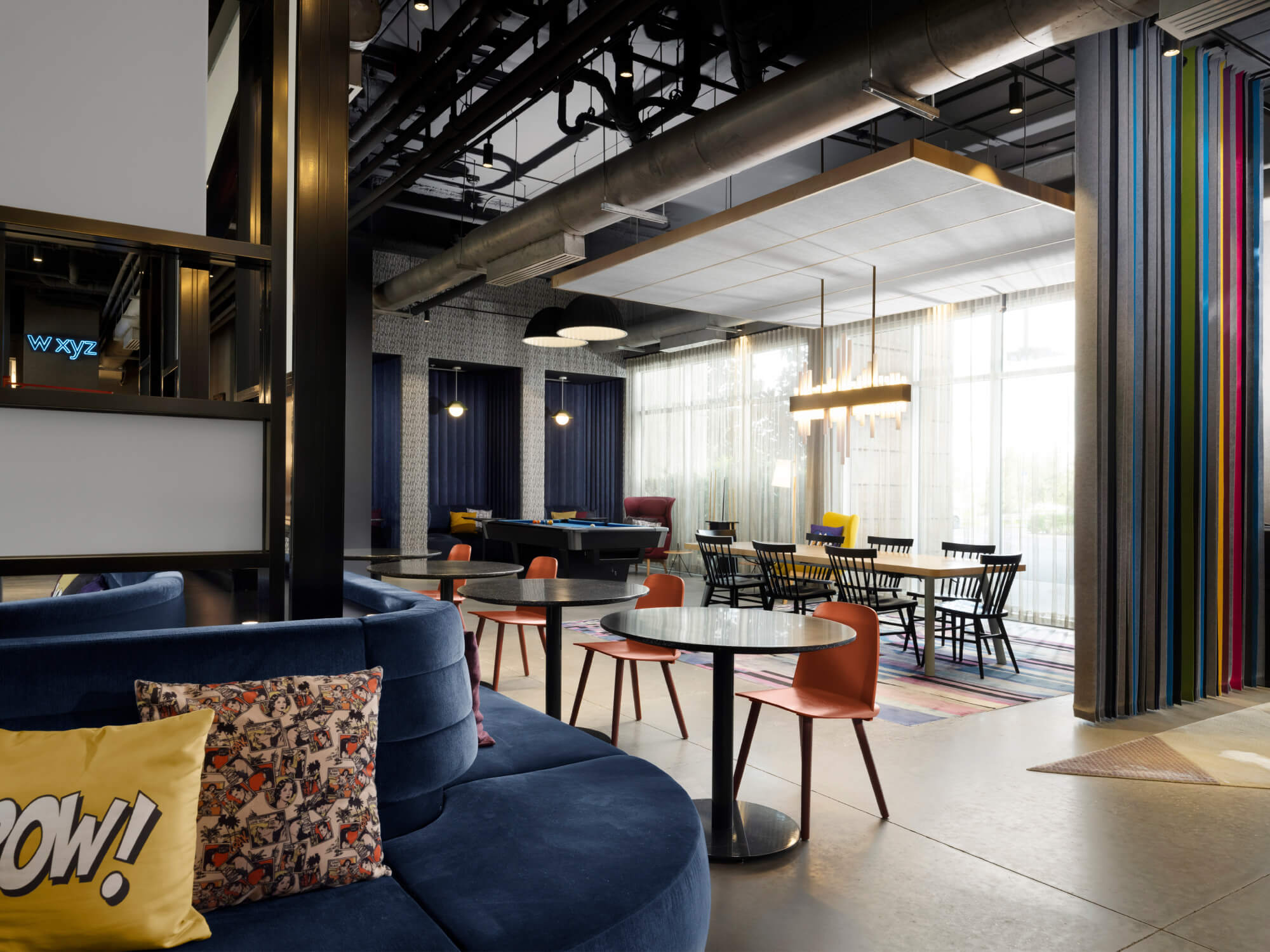 Modern lobby seating area with blue curved sofa, colorful pillows, tables, chairs, and large windows.