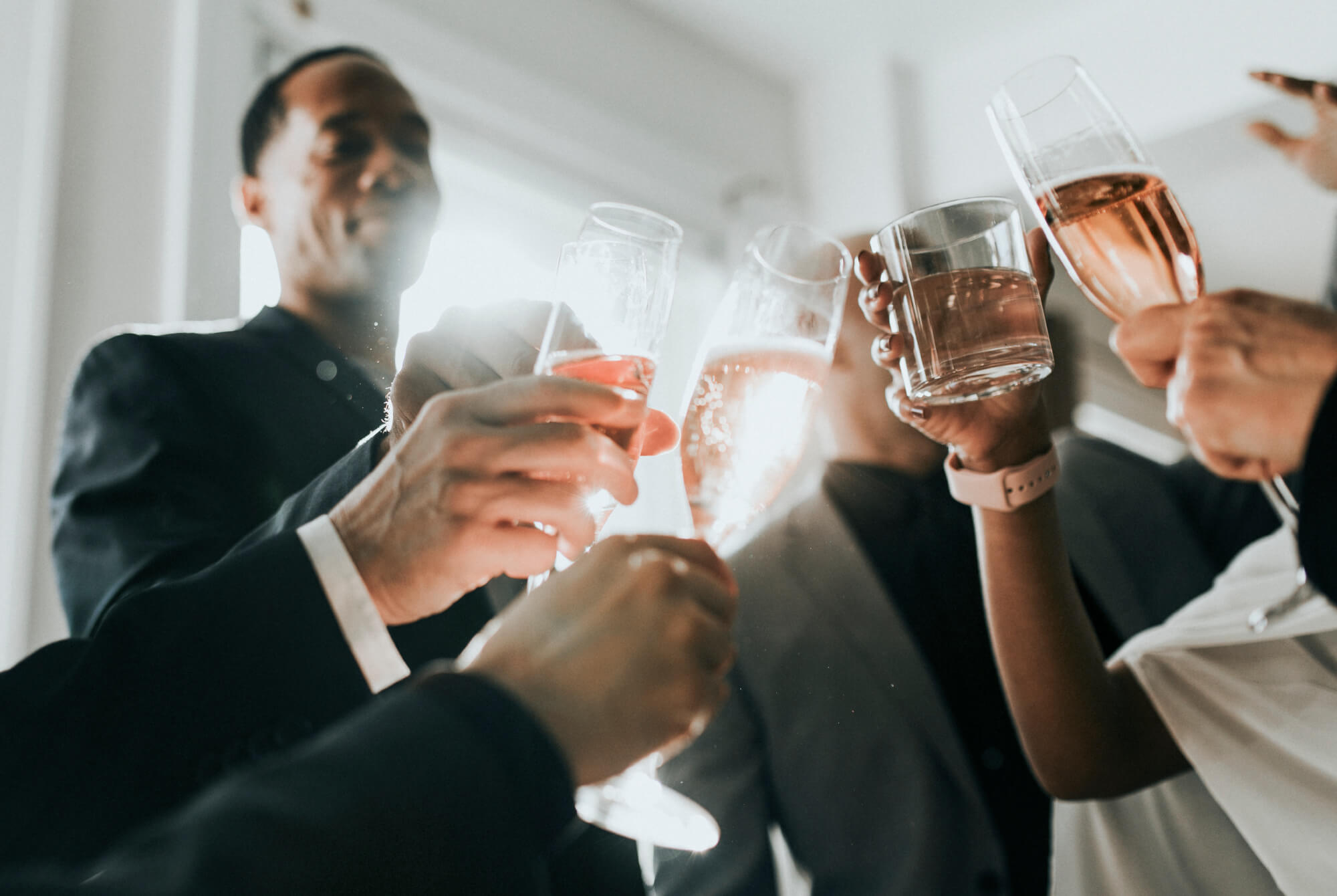 Close-up of diverse people raising glasses of wine and whiskey in a celebratory toast indoors.