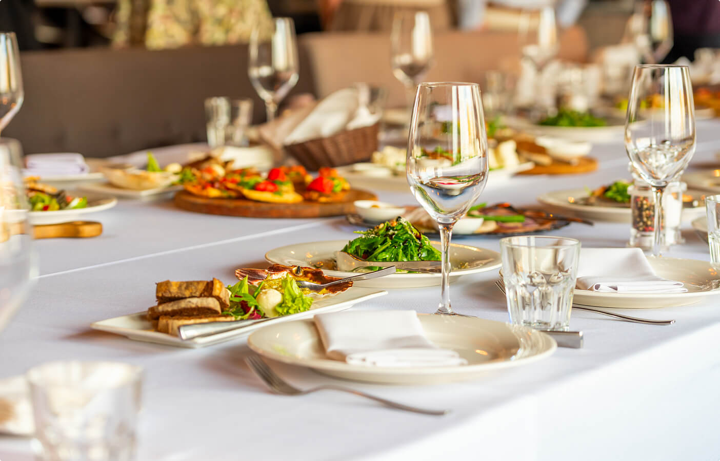 Table set for a meal with plates, napkins, glasses, cutlery, salad, and appetizers on a white tablecloth.