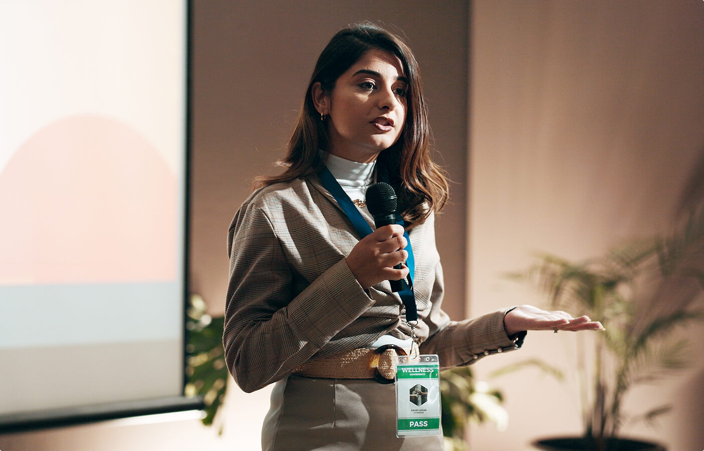 Woman with brown hair speaking at a conference holding a microphone and gesturing with her hand.