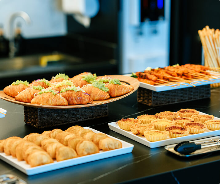 Variety of pastries and skewers arranged on trays on a black countertop.