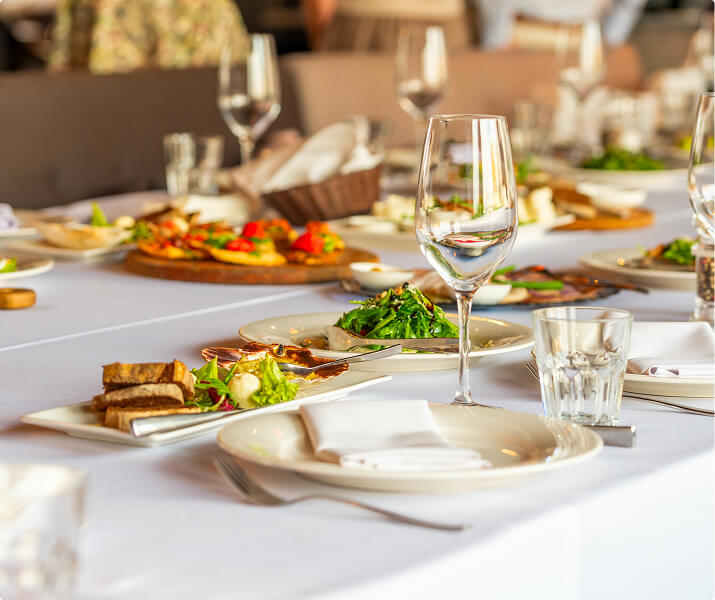 Table set for a meal with plates, glasses, salad, bread, and appetizers on a white tablecloth.