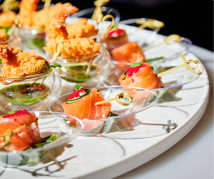 Assorted elegant appetizers with smoked salmon, caviar, and fried shrimp on a white platter.