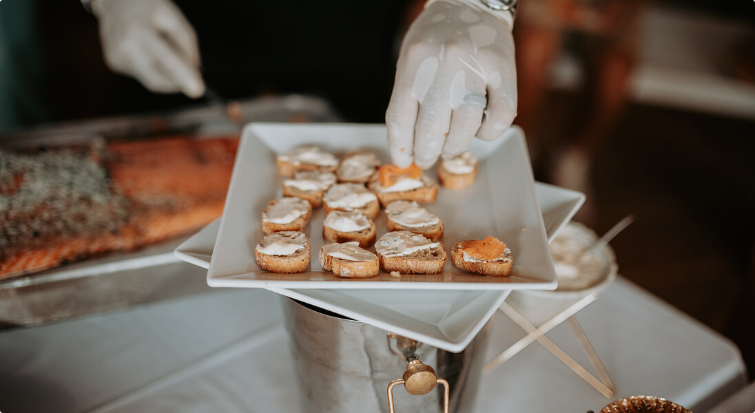Hand wearing glove placing a piece of bread with spread on a white square plate with more pieces.