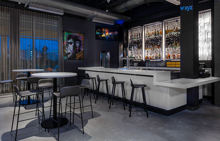 Modern bar interior with white countertops, black stools, round tables, and colorful artwork on the walls.