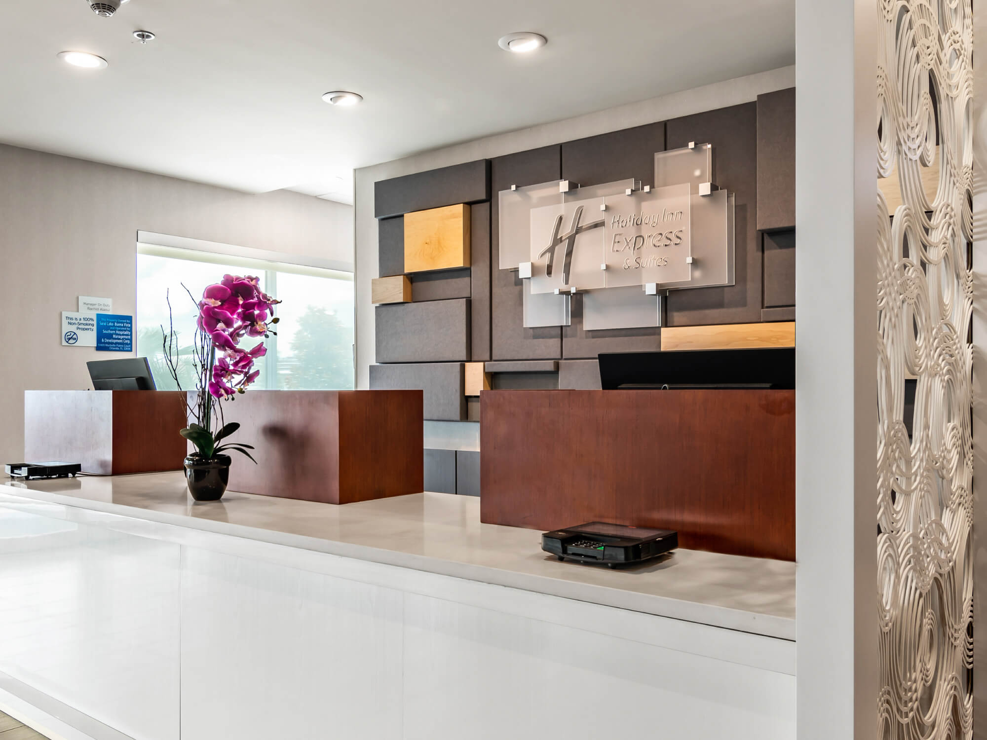 Holiday Inn Express & Suites reception desk with wooden panels and purple orchid on counter.