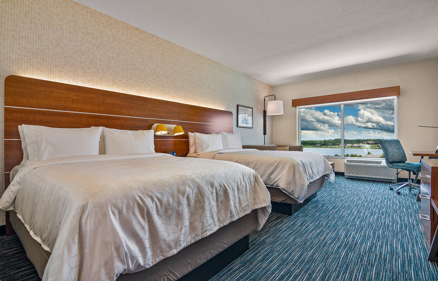 Hotel room with two queen beds, large window with lake view, desk, and blue patterned carpet.