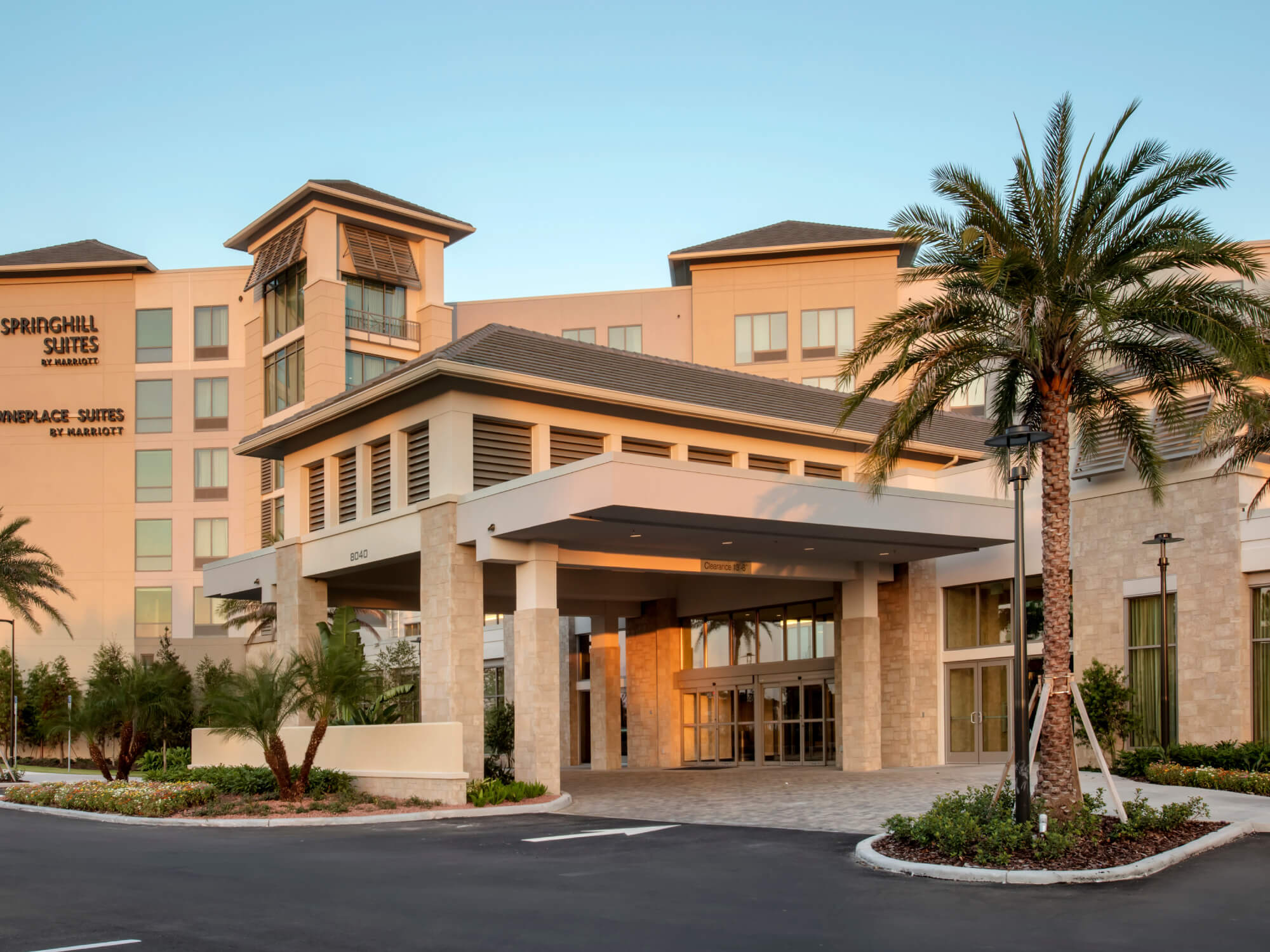 Entrance of a SpringHill Suites by Marriott hotel with palm trees and clear sky.