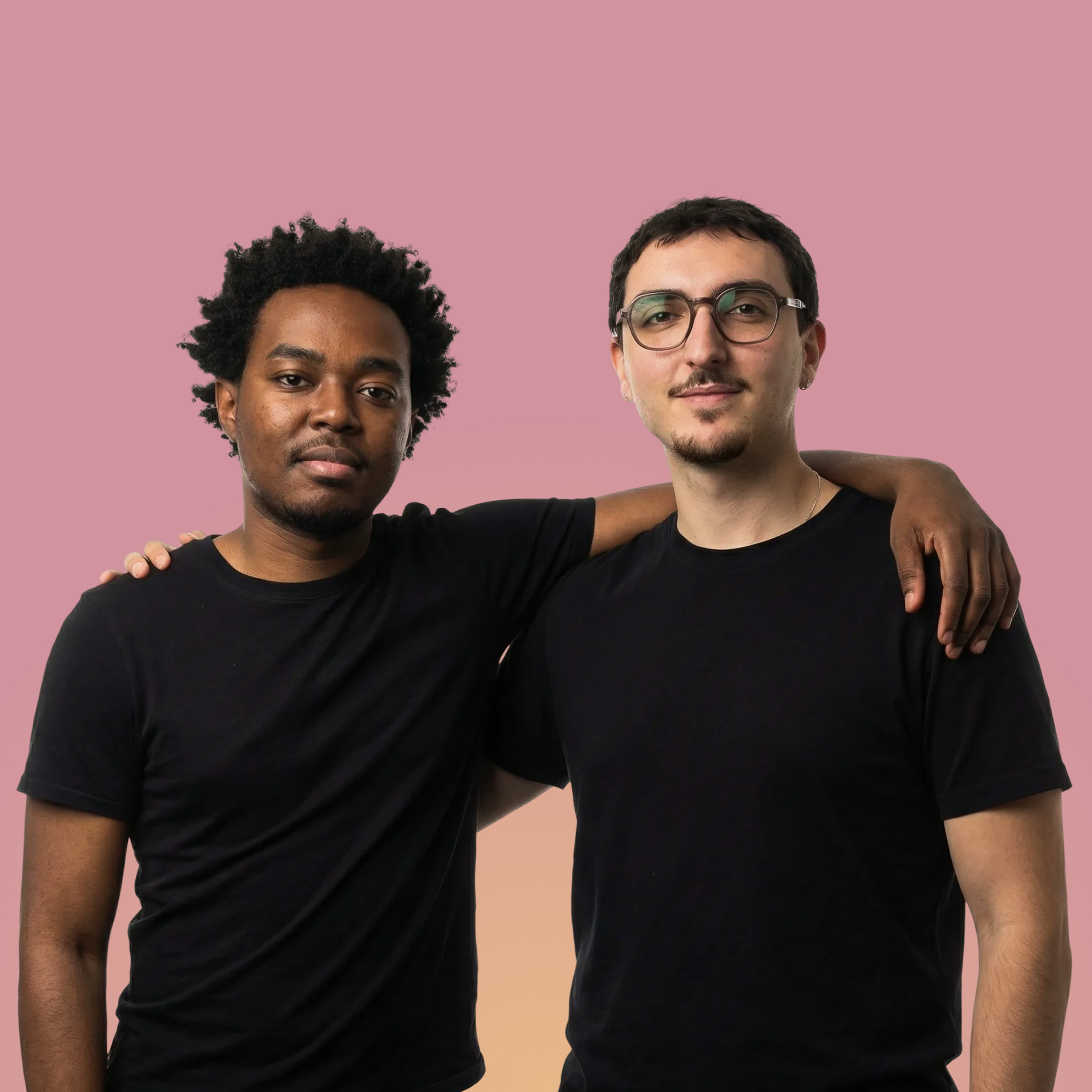 Deux hommes souriants portant des t-shirts noirs, l'un avec des lunettes et l'autre avec un bras autour de l'épaule de son ami, sur un fond dégradé rose et orange.