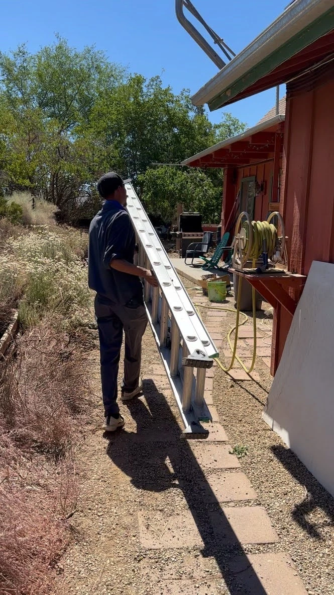 Worker carrying long metal ladder next to red barn on sunny day