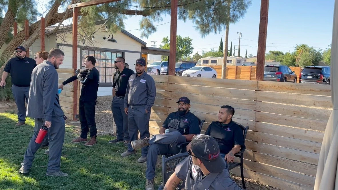 Group of workers in gray uniforms taking a break outside wooden fence