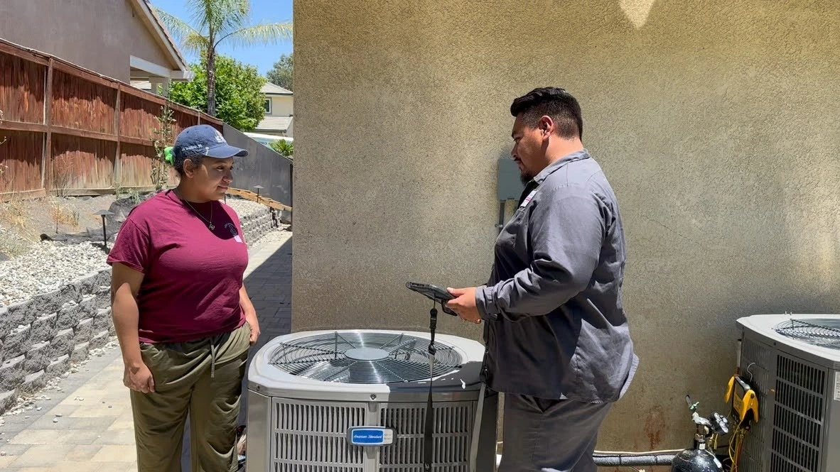 HVAC technician inspects air conditioning unit with homeowner outside