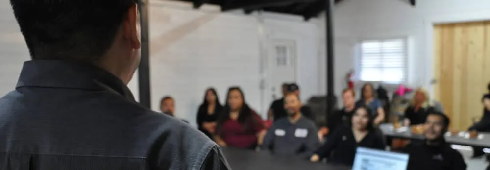 Person facing group in meeting room with blurred participants