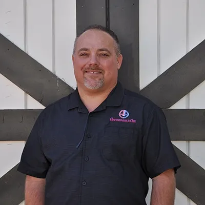 Smiling middle-aged person in dark polo shirt standing in front of striped wall