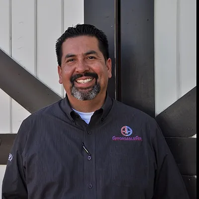 Smiling man in dark shirt with company logo standing near metal structure