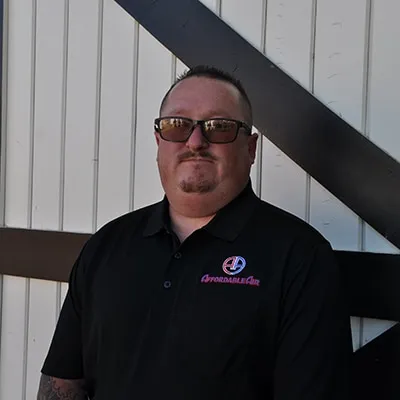 Professional wearing sunglasses and black polo shirt against white wall