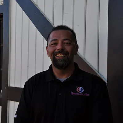 Smiling man in black polo shirt standing in front of white building