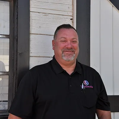Smiling middle-aged man in black polo shirt standing near white building