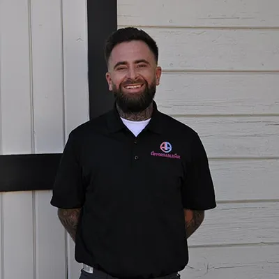 Smiling bearded man in black polo shirt standing in front of white wall
