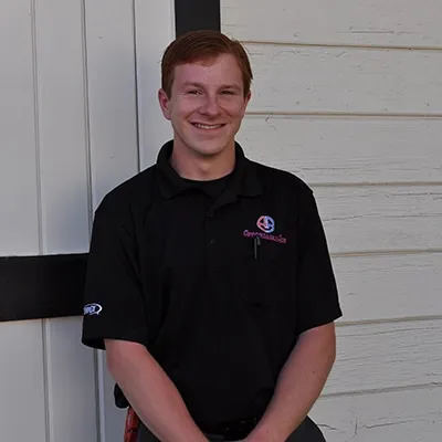 Smiling young person in black polo shirt standing against white wall