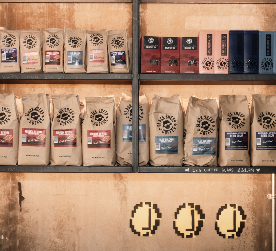 Shelves displaying Black Sheep Coffee bags and tea boxes with pixel-art coffee bean decorations on the wall below, along with pricing signage.