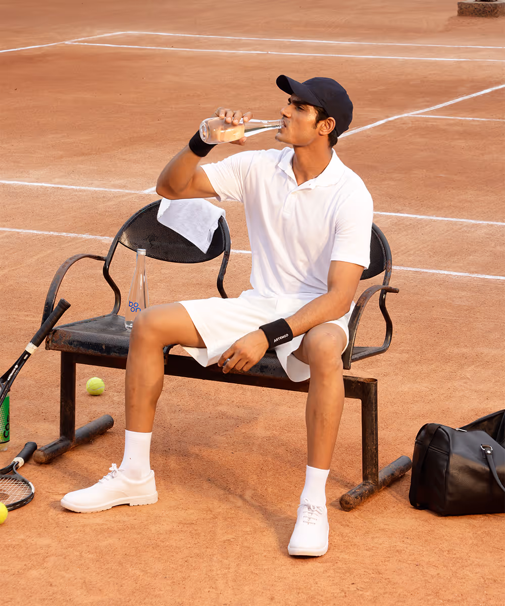 A tennis player drinking water from a boon bottle