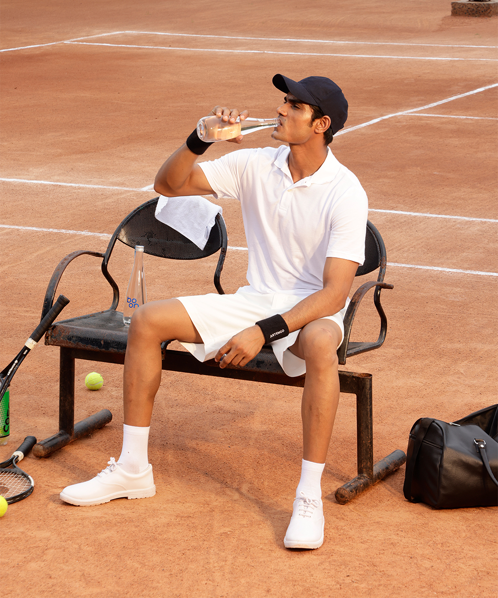 A tennis player drinking water from a boon bottle