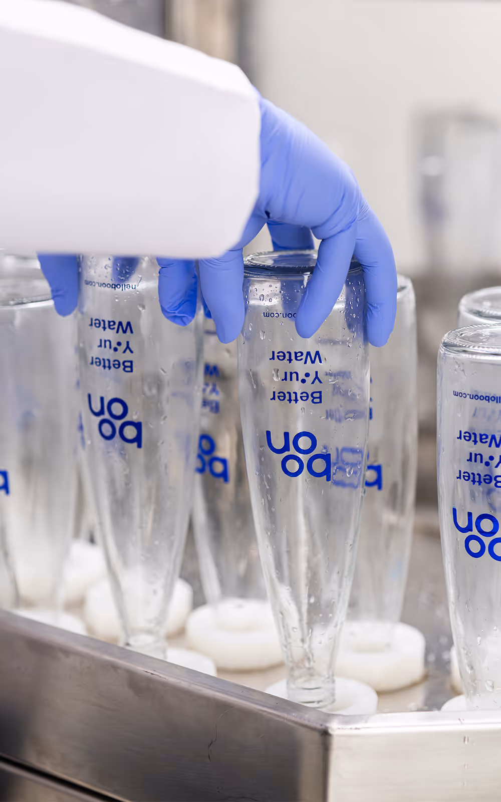 Gloved hands holding empty bottles at a washing chamber