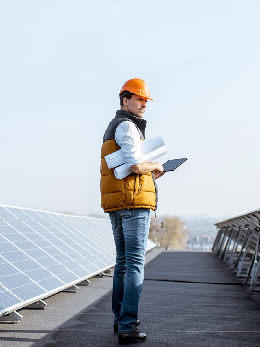 A man in a hard hat and vest standing on a roof.