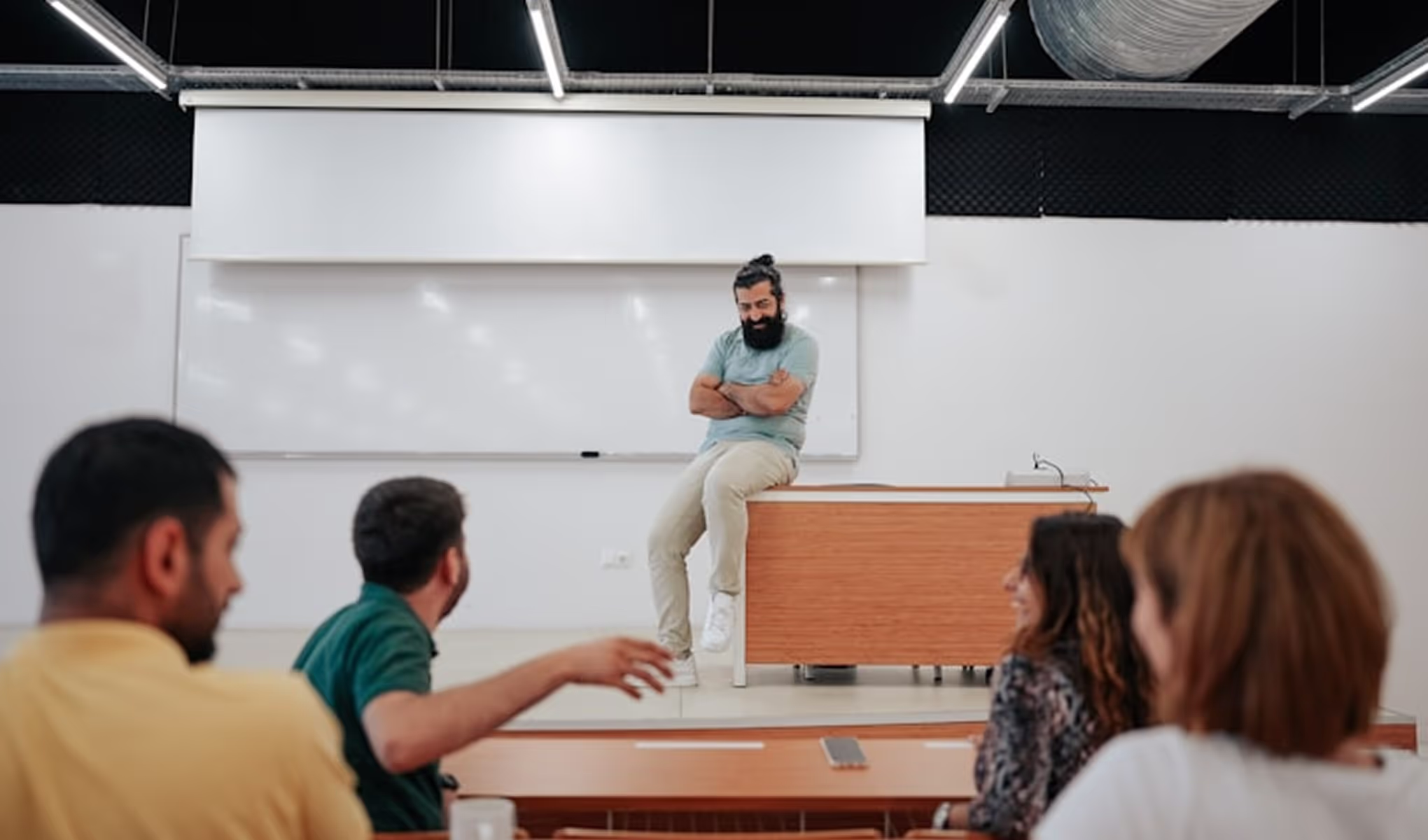 A man sitting on top of a desk in front of a group of people.