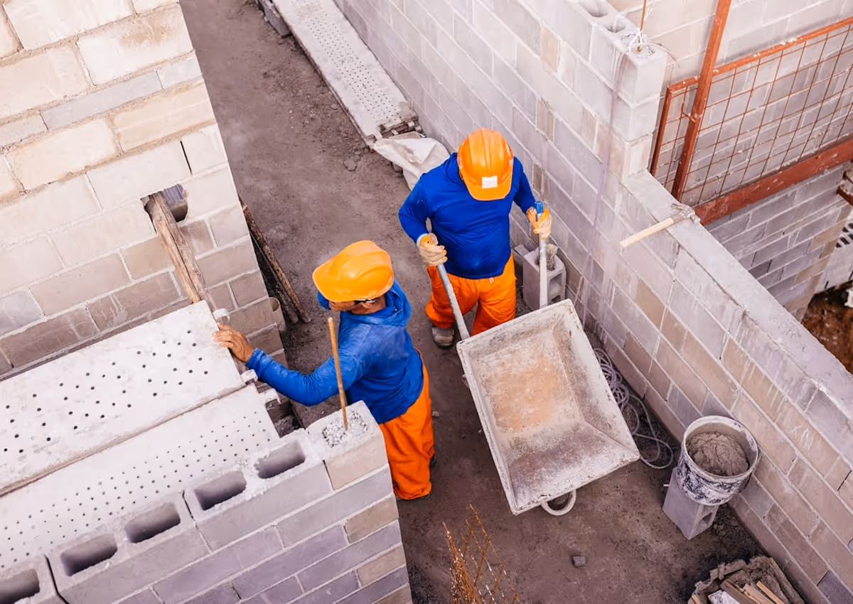 Two men in orange and blue work on a construction site.