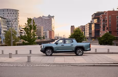 Vollelektrischer MAXUS eTERRON 9 Pick-up mit Allradantrieb, seitliche Ansicht in urbaner Umgebung mit moderner Architektur im Hintergrund – kraftvoller Elektro-Pick-up für Stadt und Gelände.