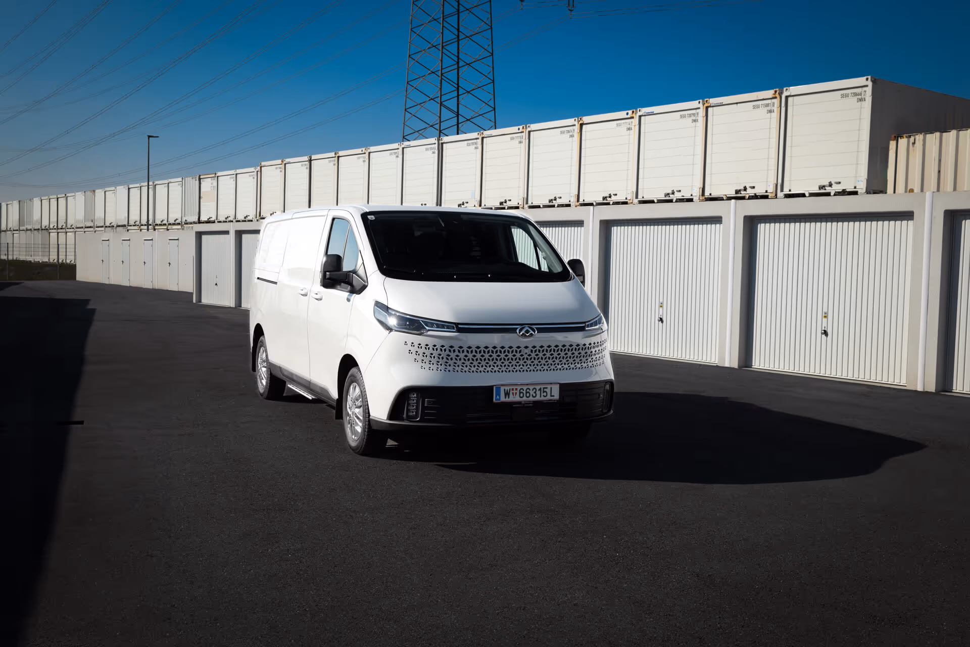 Weißer MAXUS eDELIVER 7, vollelektrischer Kastenwagen, geparkt vor Garagen in moderner Umgebung – ab sofort in Österreich verfügbar, ideal für emissionsfreie Transporte.