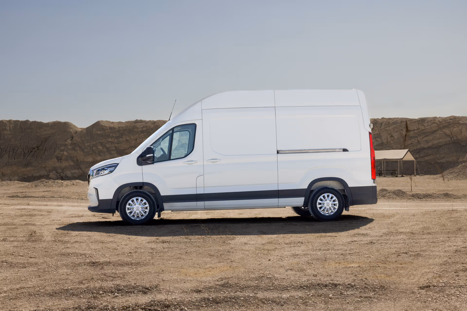 Weißer MAXUS eDELIVER 9 Kastenwagen in Seitenansicht vor sandiger Landschaft – vollelektrischer Transporter mit großem Ladevolumen für emissionsfreie Logistik und Gewerbeeinsätze.