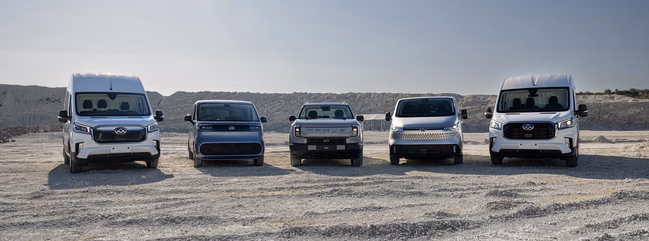 MAXUS Produktpalette 2025: vollelektrische Nutzfahrzeuge eDELIVER 3, eDELIVER 9, eDELIVER 7 und eTERRON 9 nebeneinander in Kieslandschaft – moderne Elektro-Transporter und Pick-up für Gewerbe und Alltag.