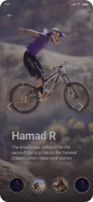 Mountain biker wearing a helmet and purple shirt performing a stunt with arms extended while balancing on the bike rear wheel.