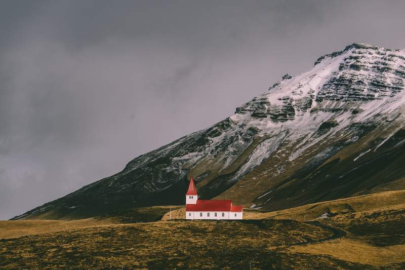 A church in a remote are of Iceland with snowy mountains in the background.