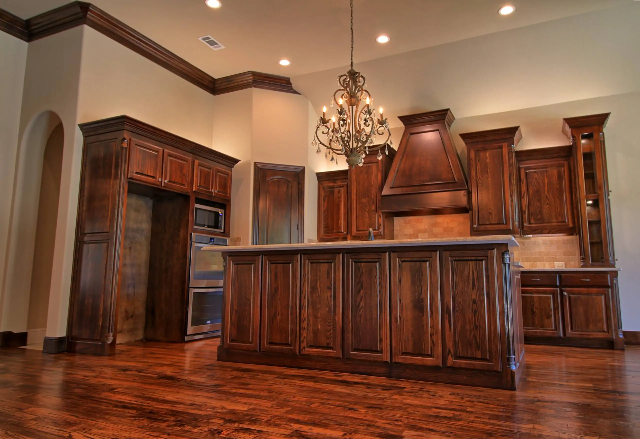 Traditional kitchen with rich dark wood cabinetry, a central island, ornate chandelier, and crown molding throughout, featuring a warm and elegant design.