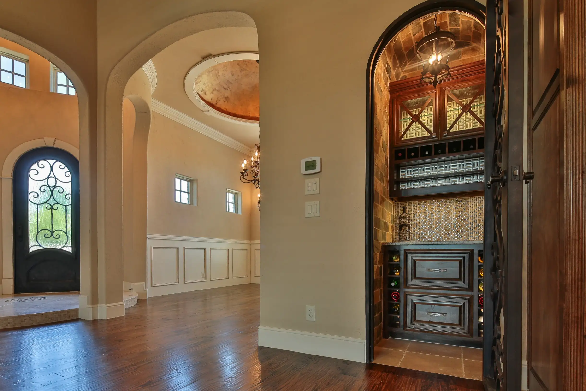 Elegant entryway with arched doorways, wood flooring, decorative ceiling detail, and a built-in wine storage nook with iron door and rich wood cabinetry.