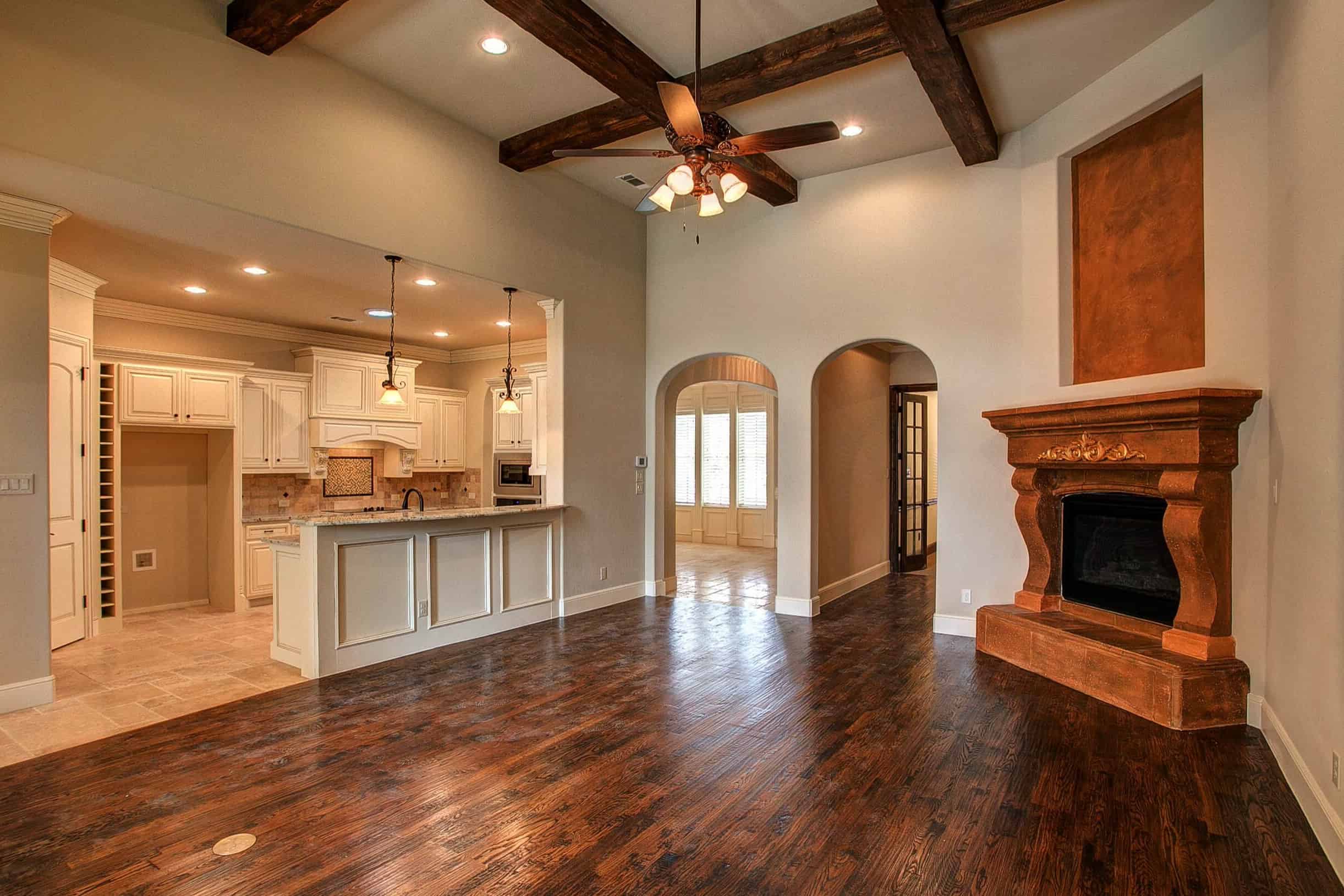 Luxury open-concept living space by Oakmark Signature Homes with rustic fireplace, wood beams, and custom kitchen with white cabinetry.