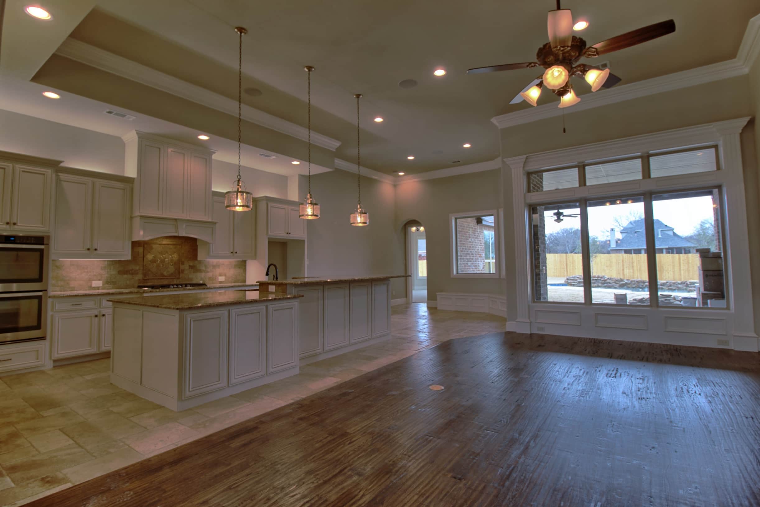 Luxury custom kitchen and living space by Oakmark Signature Homes featuring large island, pendant lighting, and open-concept design with oversized windows.